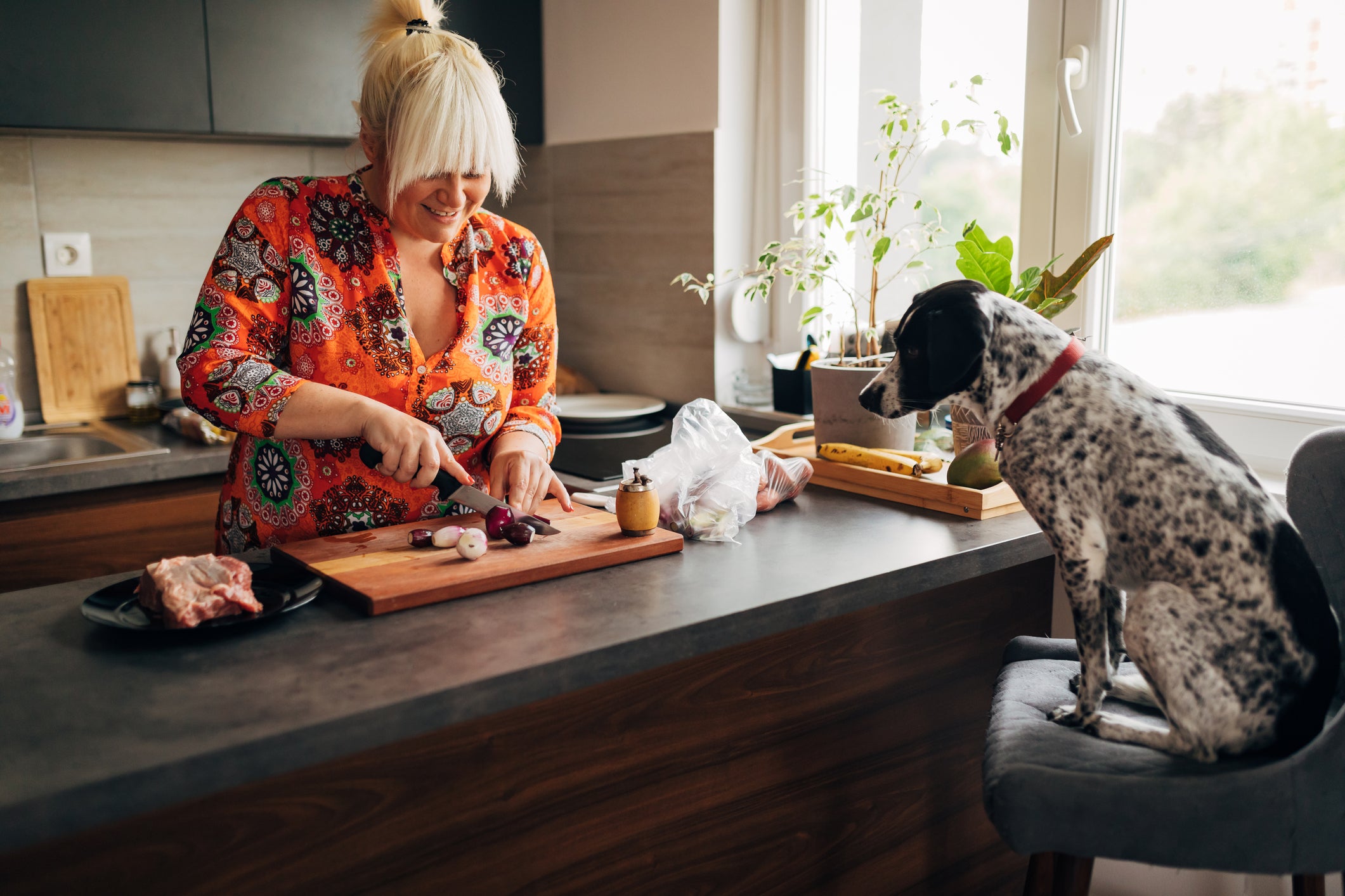 Mulher cortando carnes na cozinha enquanto cachorro a observa