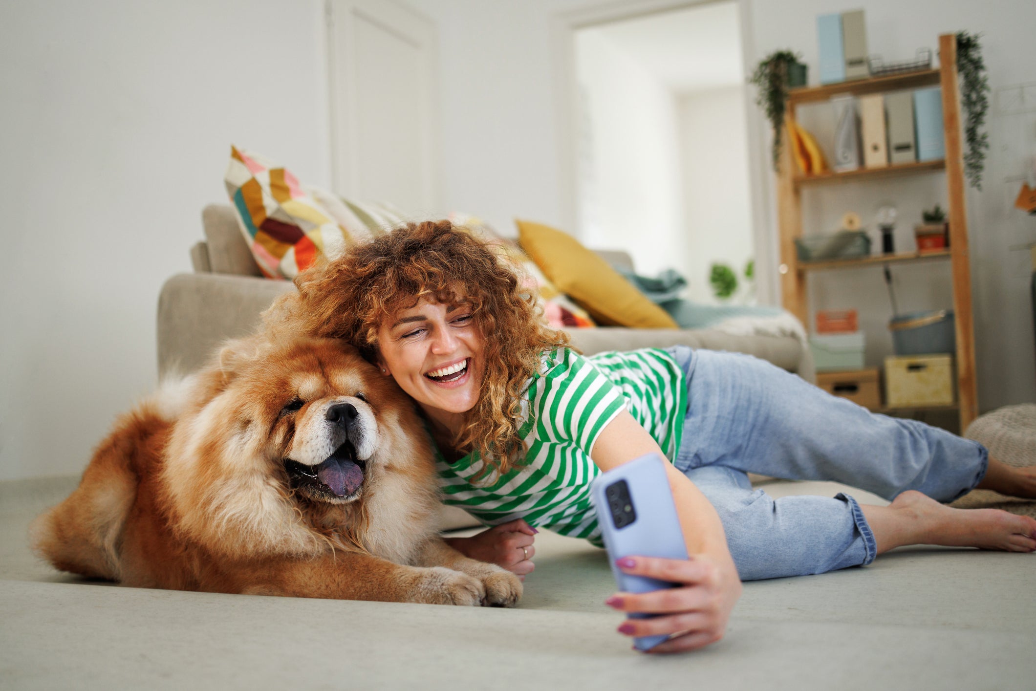 Tutora tirando "selfie" com seu cachorro Chow Chow, ambos deitados no chão de sala de estar