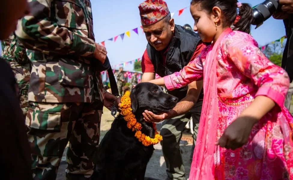 Criança e guarda fazendo cariho em um cachorro preto usando colar de flores