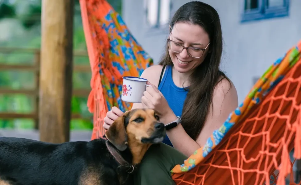 cachorro ao lado de mulher tomando café em rede