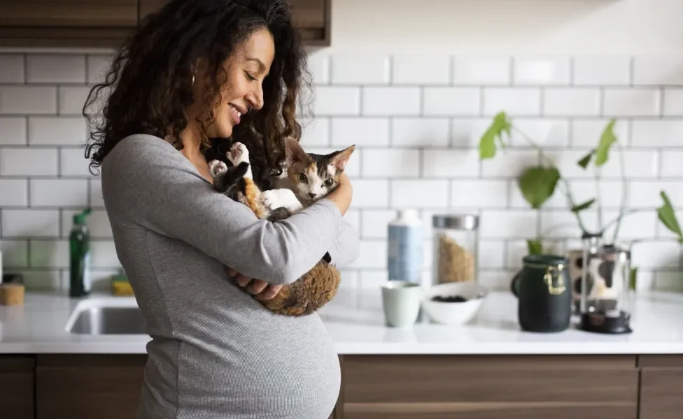 Mulher grávida segurando gato no colo enquanto sorri