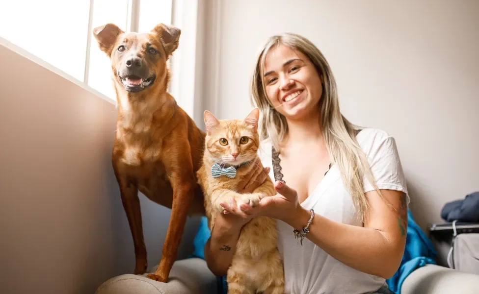 Tutora sorrindo ao lado de cachorro e gato