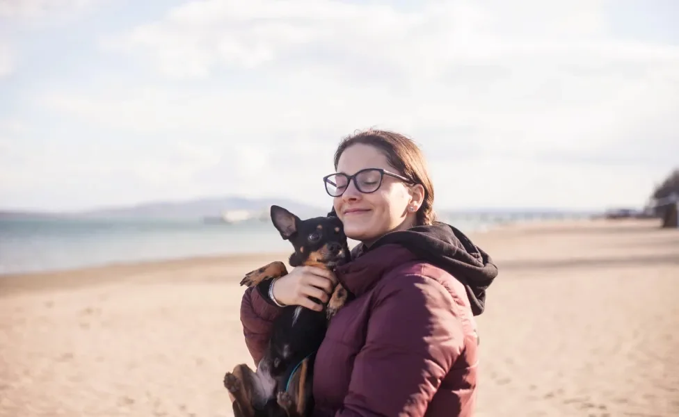 Tutora abraçando cão Pinscher em praia