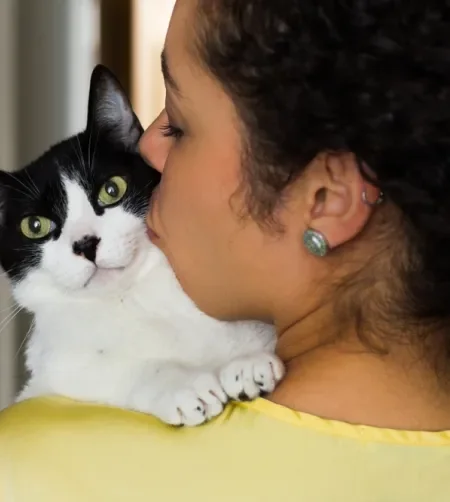 Mulher de cabelo preto de costas segurando e beijando um gato branco e preto